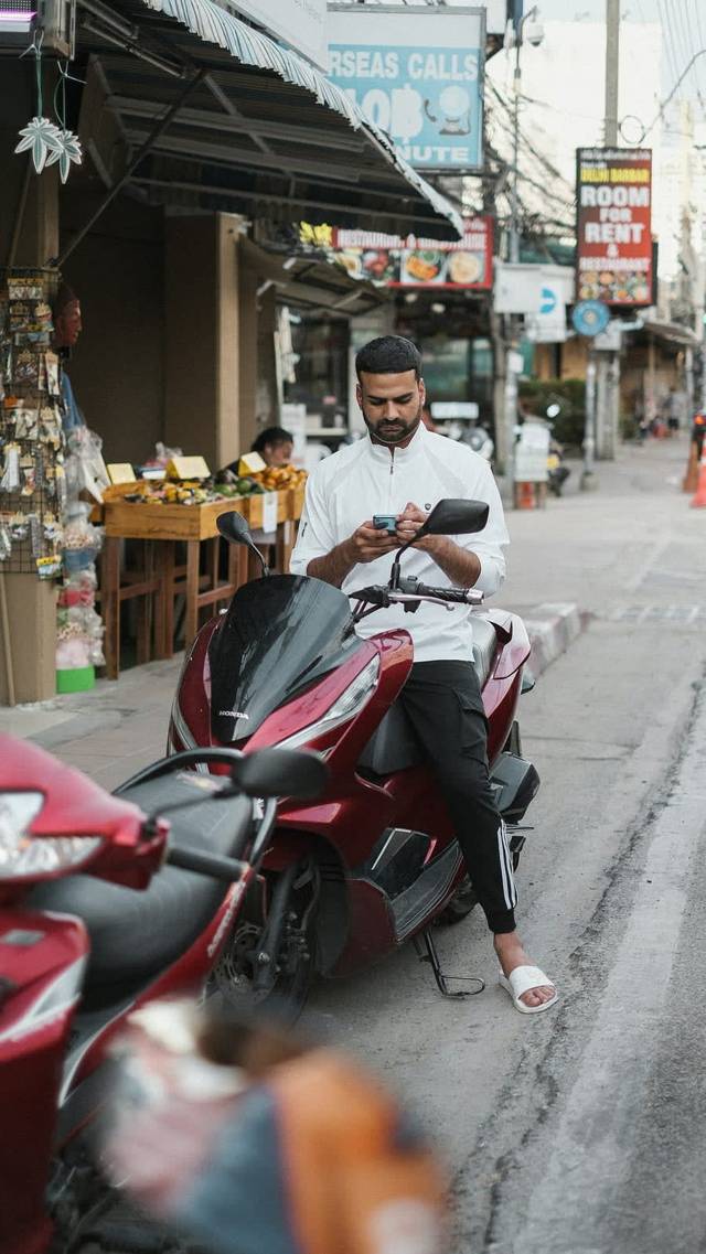 Man op een geparkeerde scooter kijkt op zijn telefoon, met een bord voor internationaal bellen erachter