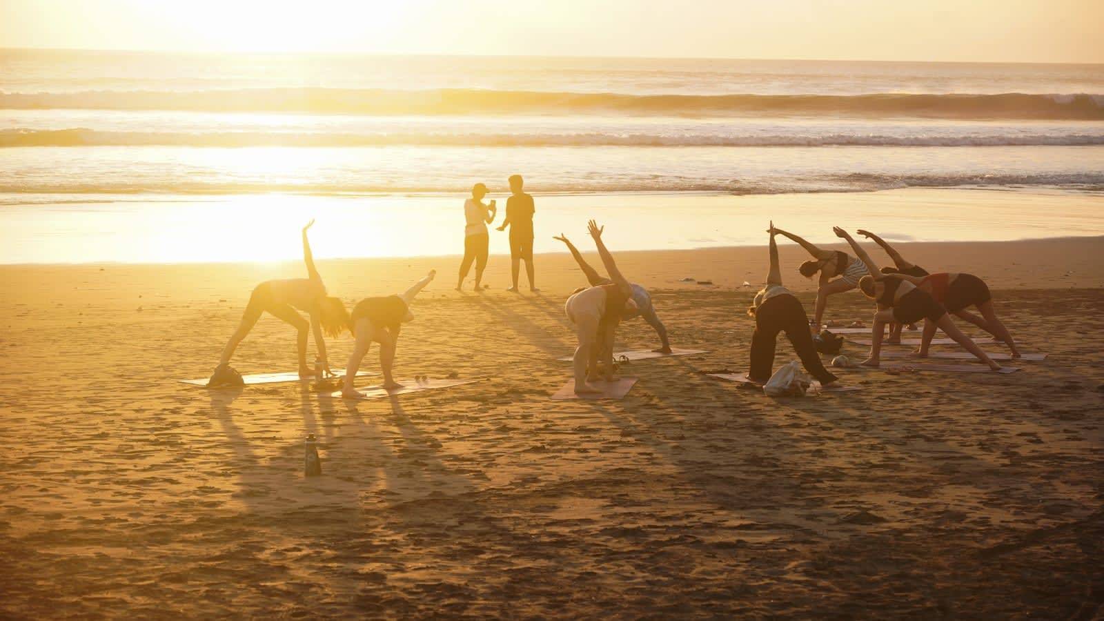 Groep die samen yoga doet op het strand bij zonsondergang