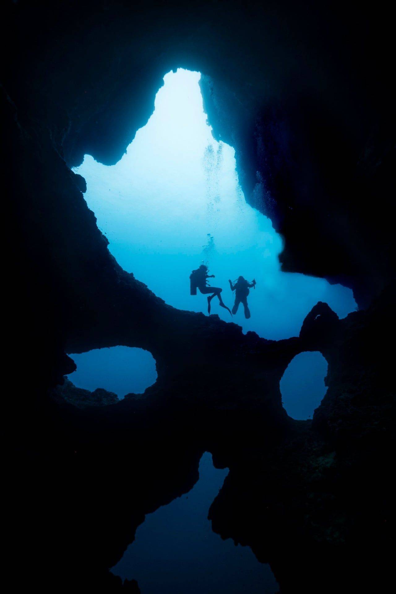 Duikers zweven onder de rotsopening van de Cathedral bij Pescador Island