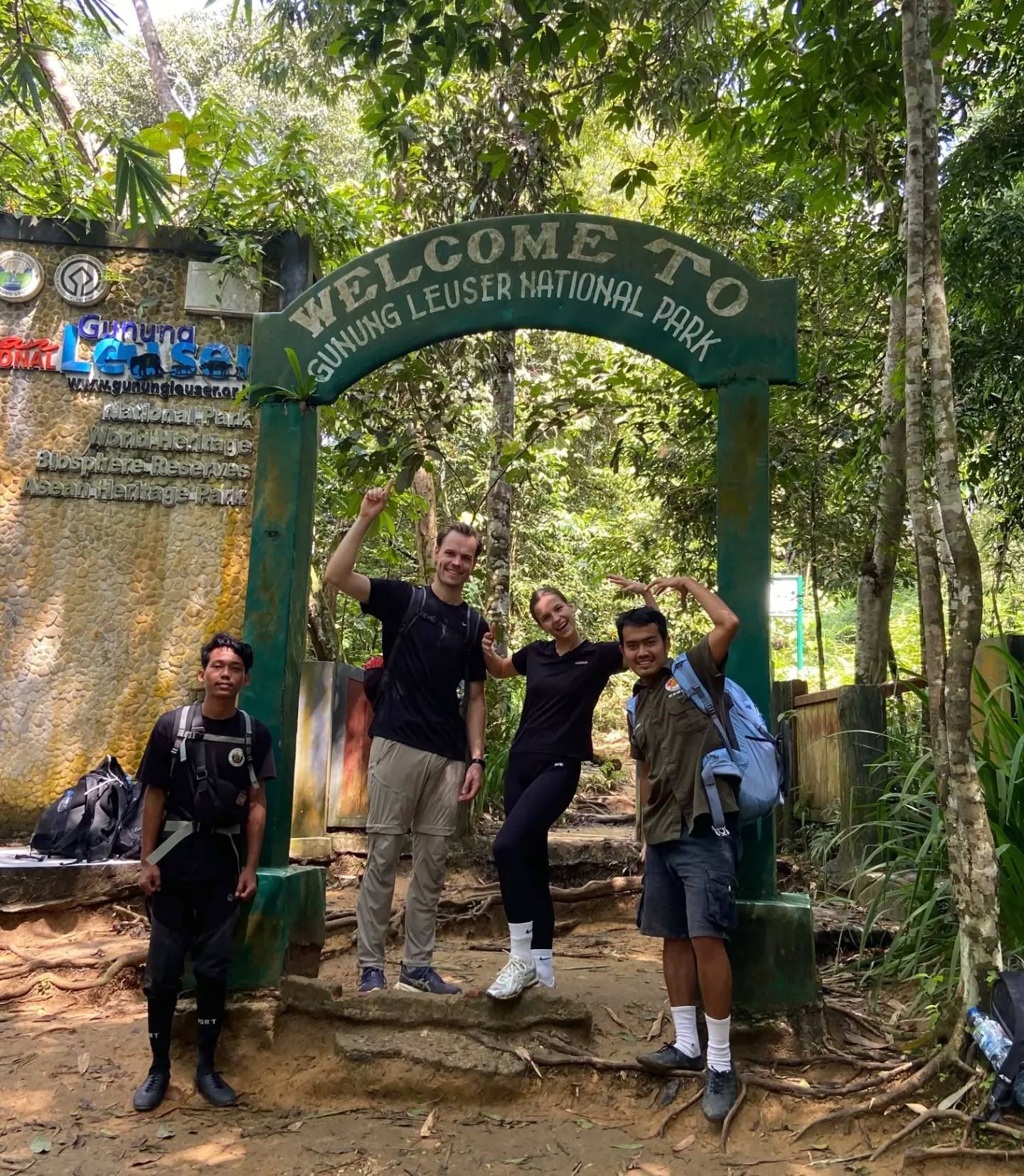 Trekkers en hun gidsen onder de groene welkomstboog van Gunung Leuser National Park