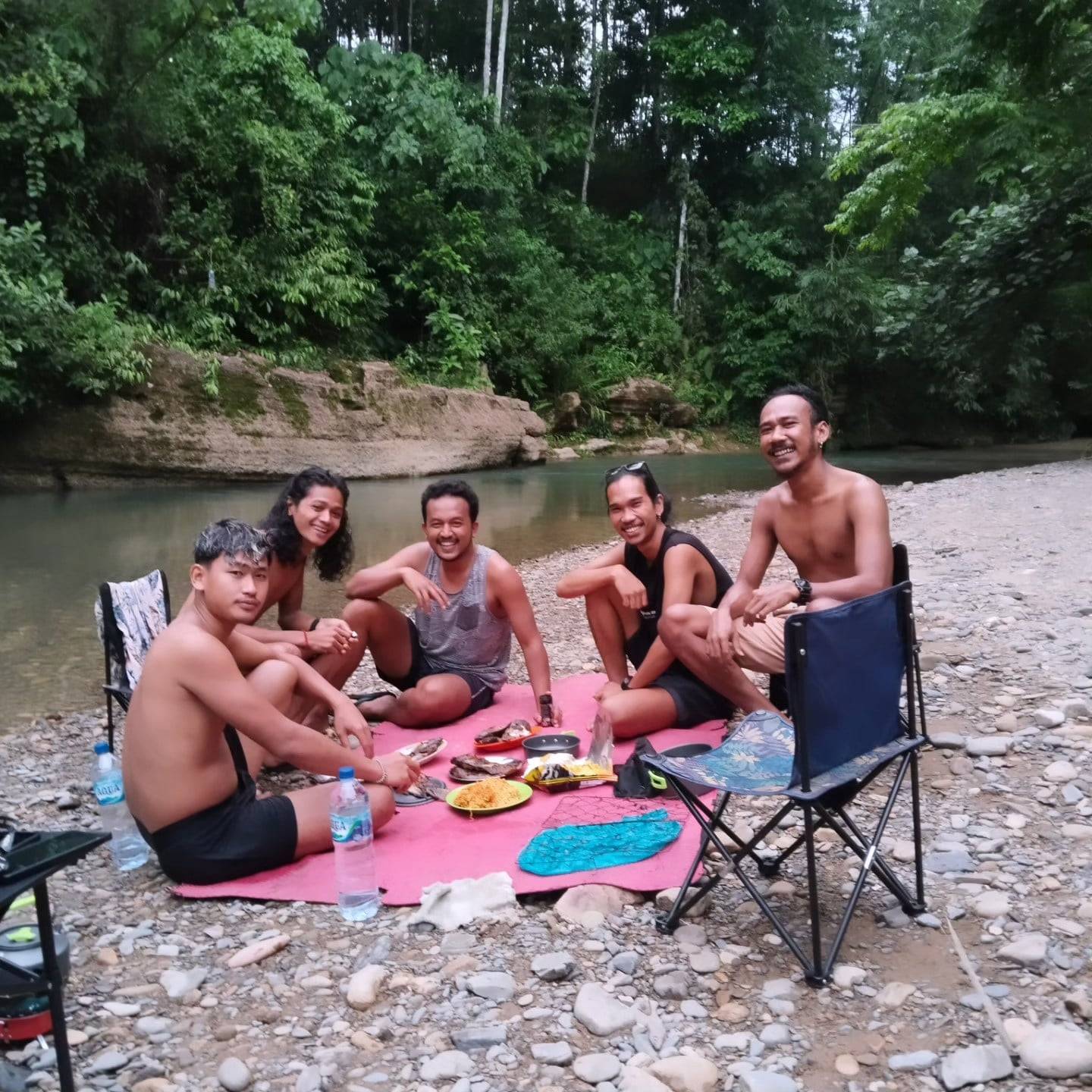 Trekkers en gidsen eten samen op een kleed op de kiezels aan de rivier