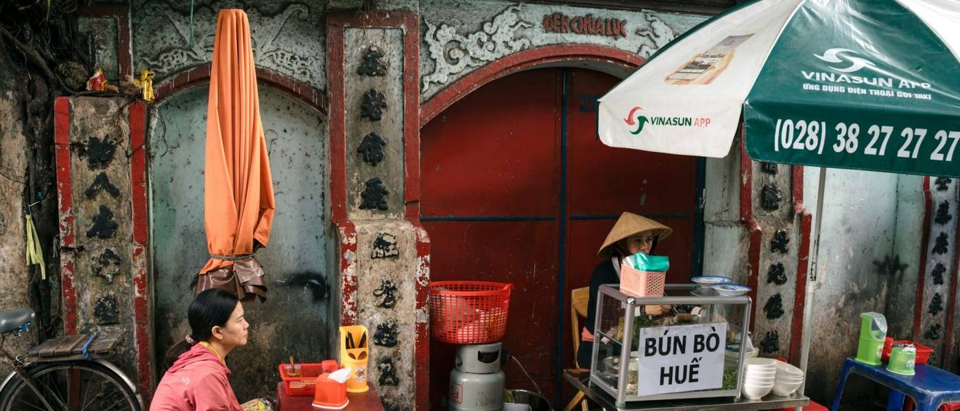 Vrouw wacht op een kom bun bo hue bij een straatkraampje in District 4