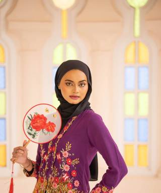 Vrouw met hoofddoek in geborduurde traditionele kleding met een waaier