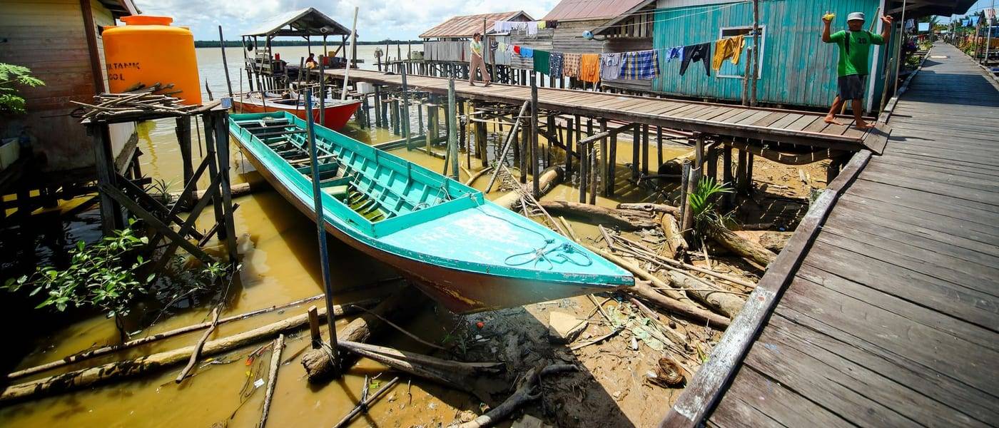 Houten paalwoningen, een loopplank en een turquoise boot in een dorp aan het water